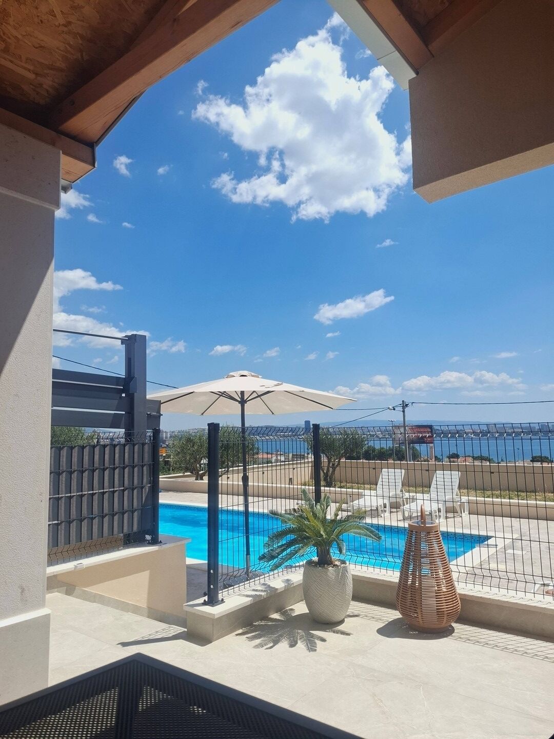 A pool area with a view of the sea, a pergola, and a fenced patio with lounge chairs.