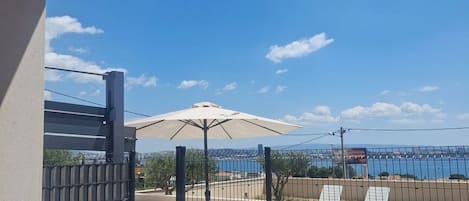 A pool area with a view of the sea, a pergola, and a fenced patio with lounge chairs.