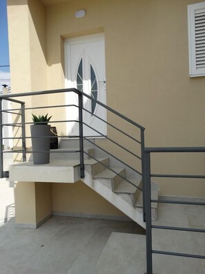 Eine Betontreppe mit Metallgeländern führt zu einer weißen Tür mit einem Fenster.