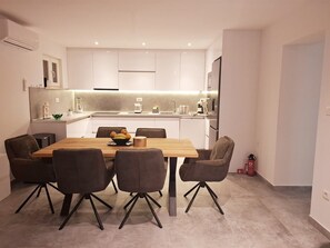 A modern kitchen with white cabinets, a wooden dining table, and four chairs. - Apartments Oliva with Shared Heated Pool / Two Bedroom Apartment with Pool (Kaštel Sućurac)