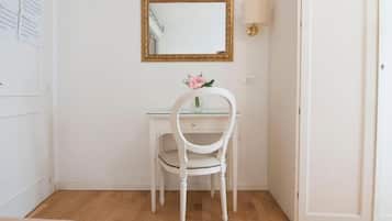 A white desk with a chair, a mirror with a gold frame, and a wall-mounted lamp.