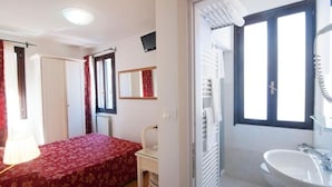Ein Schlafzimmer mit Bett, Stuhl, Schreibtisch, Spiegel, Fenster und einem Badezimmer mit Waschbecken.
