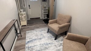 Una sala de estar con un sillón beige, una consola blanca, una alfombra y una puerta con ventanal.