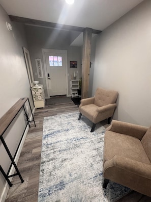 A living room with a beige armchair, a white console table, a rug, and a door with a window.
