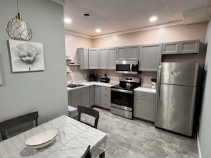 A modern kitchen with grey cabinets, stainless steel appliances, a marble countertop, and a dining area with a white table and chairs.