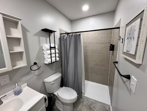 A bathroom with a toilet, sink, shower, towel rack, and a framed picture on the wall.