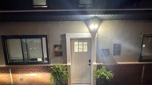 Un edificio con una puerta, dos plantas en macetas, un muro de ladrillo y una ventana.