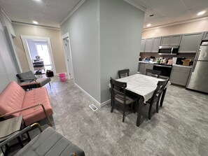 A modern kitchen with stainless steel appliances, a dining area with a table and chairs, and a living area with a sofa and armchairs.