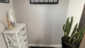 Un pasillo con un perchero negro fijado a la pared, un estante blanco, una planta en maceta y una alfombra negra.
