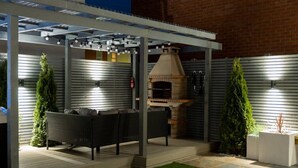 An outdoor patio with a built-in pizza oven, a seating area with a sofa and chairs, and a pergola with string lights. - Exclusive House with Canadian Hot Tub (Great Yarmouth)
