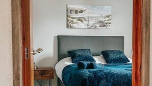 A bedroom with a bed, a nightstand, a lamp, and a painting on the wall. - Exclusive House with Canadian Hot Tub (Great Yarmouth)