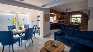 A modern living room with a blue sofa, dining area with blue chairs, and a kitchen with brick walls. - Exclusive House with Canadian Hot Tub (Great Yarmouth)