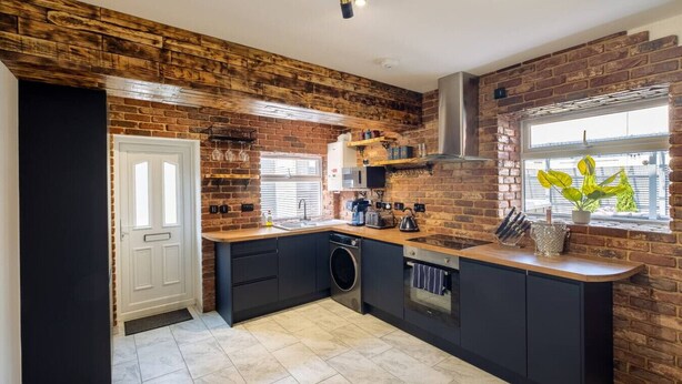 A kitchen with a brick wall, a window with a view, a sink, and a stove. - Exclusive House with Canadian Hot Tub (Great Yarmouth)