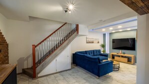 A modern living room with a blue sectional sofa, a wooden TV stand, and a staircase with a wooden railing. - Exclusive House with Canadian Hot Tub (Great Yarmouth)