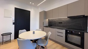 Een moderne keuken met een ronde eettafel en stoelen, een ingebouwde oven en grijze keukenkastjes.