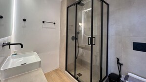 Een moderne badkamer met een douchecabine van glas, een witte wastafel en een handdoekrek.