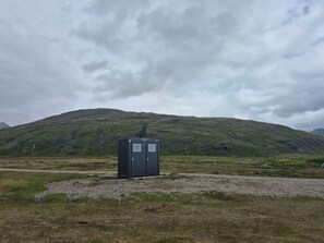 Un baño portátil en un campo de césped con una montaña al fondo.