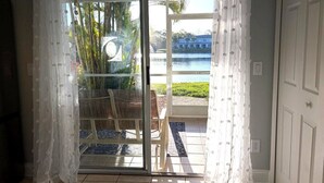 Ett rum med en skjutdörr i glas som leder ut till en uteplats med utsikt över palmer och en vattenyta.