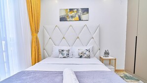 Hotellihuone, jossa on sänky, geometrisin kuvioin koristeltu pääty, yöpöytä, jossa on veistos, ja seinällä oleva taulu.