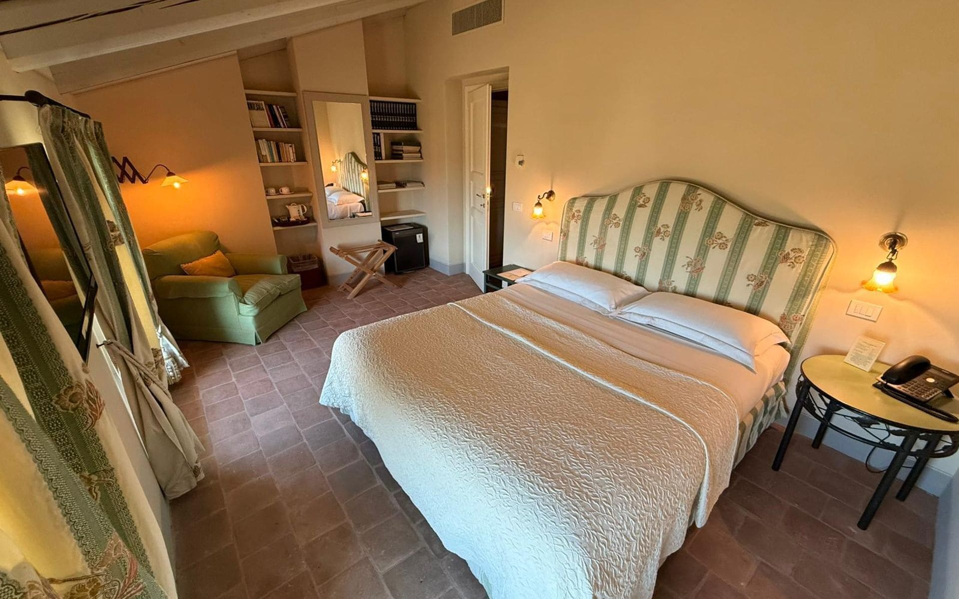 Ein Schlafzimmer mit einem großen Bett, einem Sessel, einem Schreibtisch mit Telefon und einem Bücherregal.