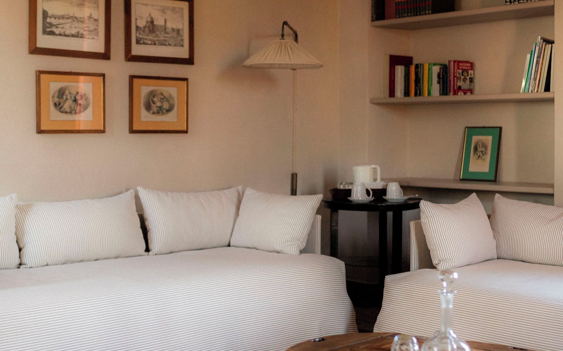 A hotel room with a sofa set, a small table with a lamp, and a bookshelf with books and framed pictures.
