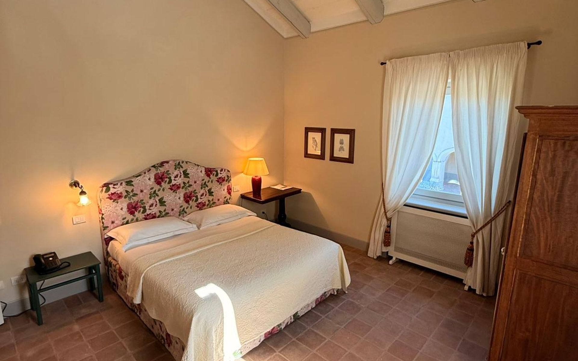A bedroom with a bed, bedside lamp, wall-mounted light, and a window with curtains.
