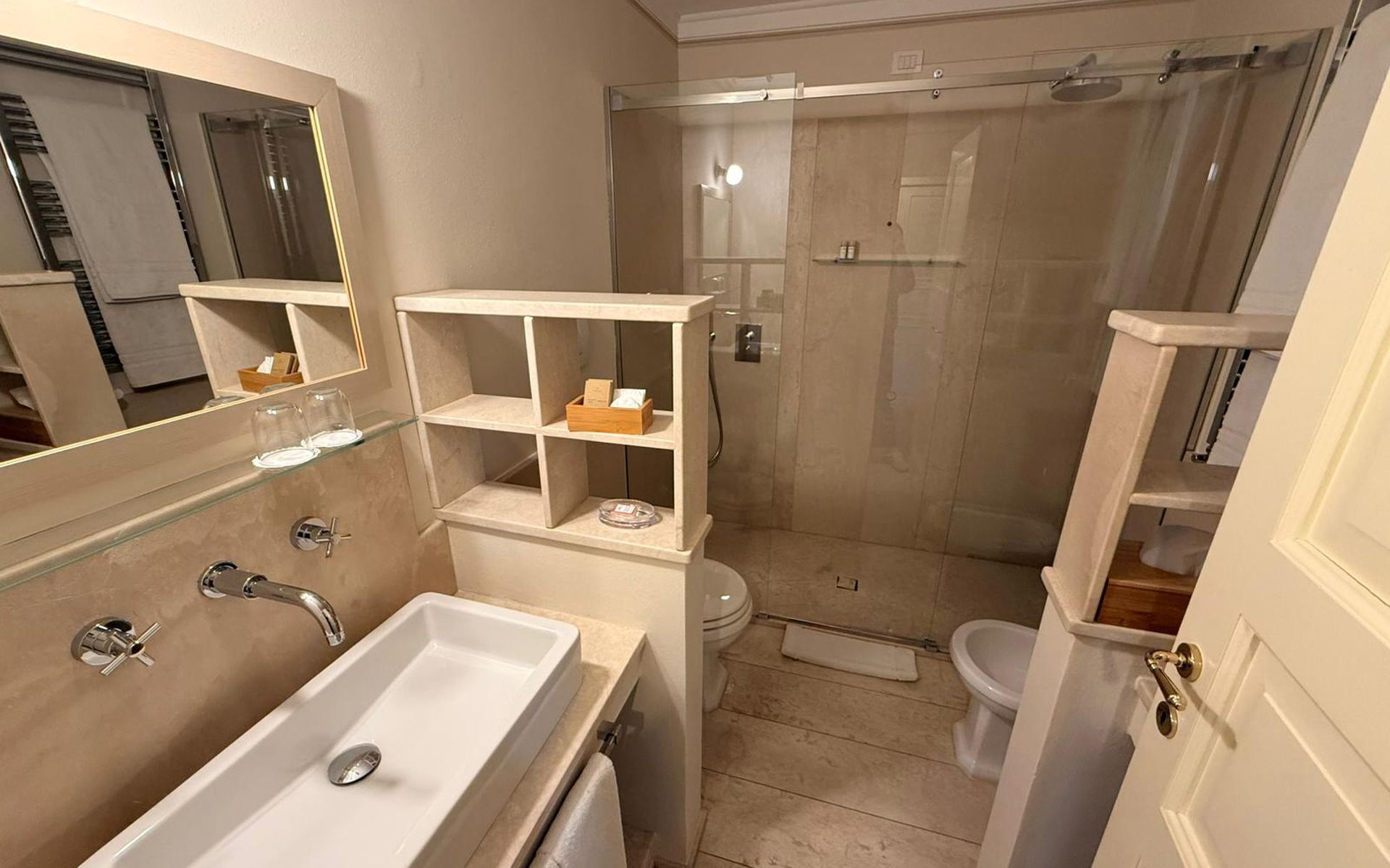 Casa de banho com lavatório, espelho, prateleiras e área de duche.
