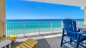 A balcony with a view of the ocean, a white table, blue and yellow chairs, and a patterned rug. - Tropic Winds 1105 (Panama City Beach)