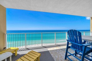 Ein Balkon mit Blick auf den Ozean, einem weißen Tisch, blauen und gelben Stühlen und einem gemusterten Teppich.