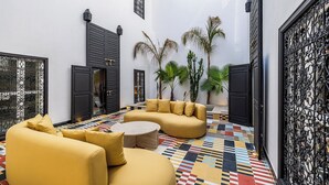 A courtyard with a yellow sofa set, a round coffee table, and potted plants. - Incredible RIAD in the heart of the Medina (Marrakech)