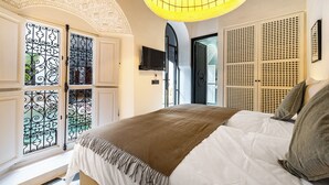 A bedroom with a bed, a TV, a decorative ceiling, and a window with wrought iron gates. - Incredible RIAD in the heart of the Medina (Marrakech)