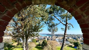 A balcony with a wrought iron railing, a brick archway, and a view of a town with houses and a body of water. - House with Balcony and Sea View in La Richardais (La Richardais)