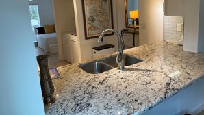 A kitchen with granite countertops, a stainless steel sink, and a map of Florida on the wall. - Update and Immaculate, 2 beds 2 baths end unit. On Imperial Golf Course (Naples)
