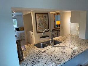 A kitchen with granite countertops, a stainless steel sink, and a map of Florida on the wall. - Update and Immaculate, 2 beds 2 baths end unit. On Imperial Golf Course (Naples)