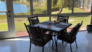 A conservatory with a table and chairs, large windows, and a view of a lake and buildings. - Update and Immaculate, 2 beds 2 baths end unit. On Imperial Golf Course (Naples)