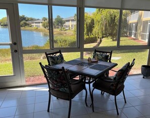 A conservatory with a table and chairs, large windows, and a view of a lake and buildings. - Update and Immaculate, 2 beds 2 baths end unit. On Imperial Golf Course (Naples)