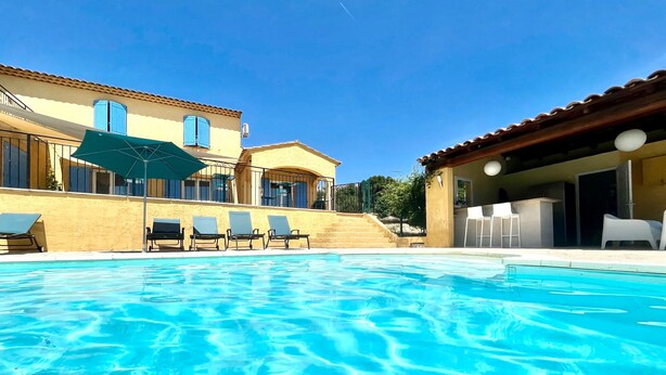 A swimming pool with lounge chairs, a covered seating area, and a building with a tiled roof. - Maison Des Arches Mérindol, spacious and bright. 6 bedrooms, private pool. (Mérindol)