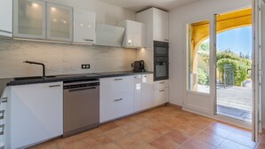 A modern kitchen with white cabinets, a dishwasher, an oven, and a coffee maker. - Maison Des Arches Mérindol, spacious and bright. 6 bedrooms, private pool. (Mérindol)