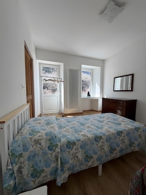 Un dormitorio con cama, cómoda, radiador y ventana con vista a árboles.