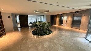 A modern lobby with a central plant, elevators, and a glass door leading outside. - APTO MORROS KAI CON SALIDA AL MAR  (Cartagena)