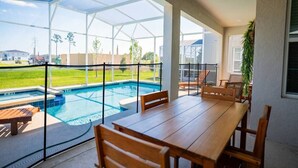 Un portico coperto con piscina, tavolo e sedie in legno e vista sulla zona circostante.