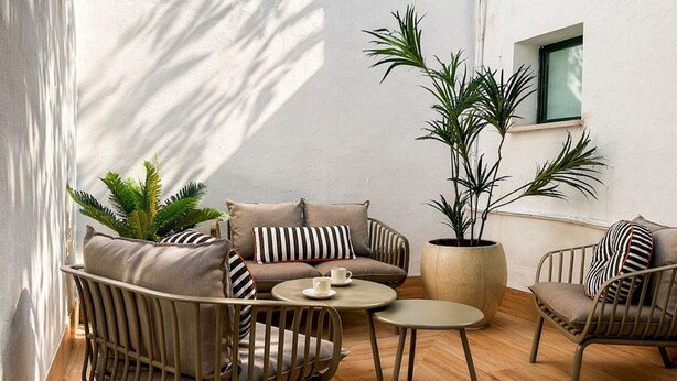 Um pátio iluminado pelo sol com um sofá, cadeiras, uma mesa de centro e plantas em vasos.