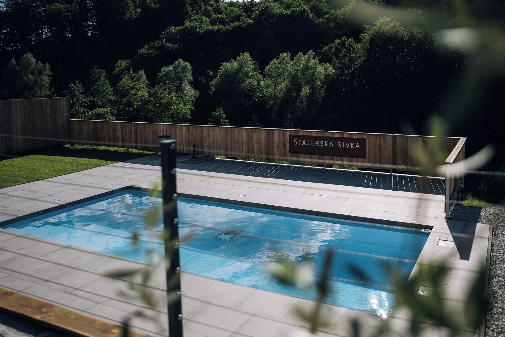 A swimming pool with a wooden fence and a sign that reads 'ŠTAJERSKA SIVKA RESORT 5.'
