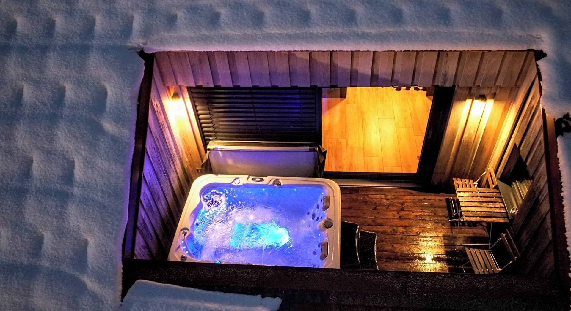 Un bain à remous installé dans un espace extérieur enneigé, avec un sol en bois et un banc.