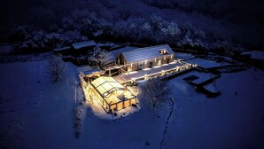 A snow-covered barn with a lit interior, surrounded by trees and a snow-covered landscape. - Lavender Retreat | With Jacuzzi and Sauna (Kamnica)