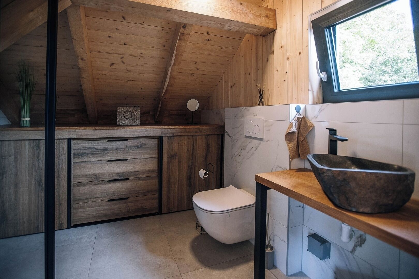 A compact bathroom with a wooden ceiling, a white toilet, a marble backsplash, and a stone sink.
