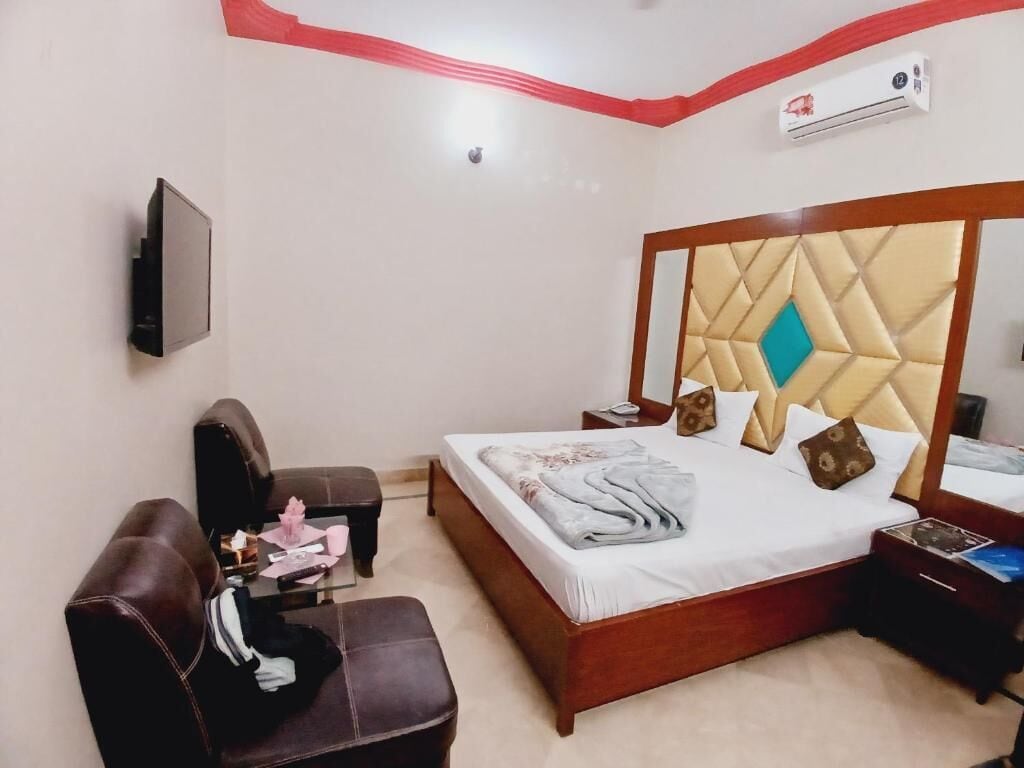 A hotel room with a bed, a desk, a chair, an air conditioner, and a TV mounted on the wall.