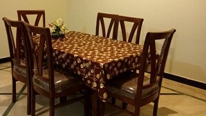 Ein Esszimmer mit einem rechteckigen Tisch, der mit einer gemusterten Tischdecke bedeckt ist, umgeben von Holzsesseln.