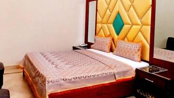 Un dormitorio con cabecera de madera, cama con colcha estampada, mesita de noche y velador.