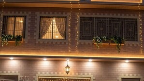 Ein Hotel Eingang mit einer Doppeltür, einem Schild mit der Zimmernummer A-24 und einer kleinen Außenbereich-Sitzgelegenheit mit Bänken und Blumentöpfen.
